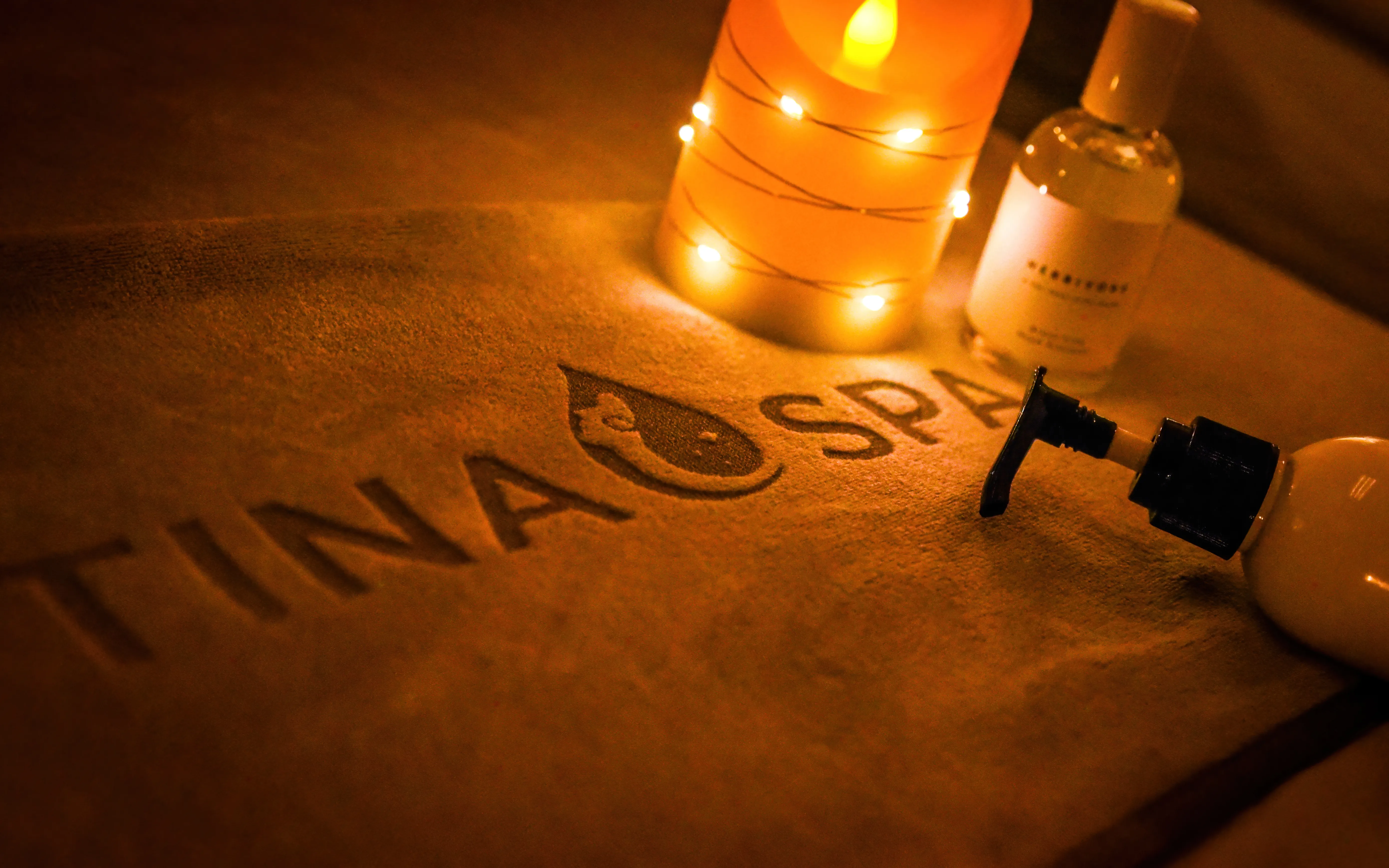 Folded Tina Spa towel with massage oil and a candle, prepared for a session